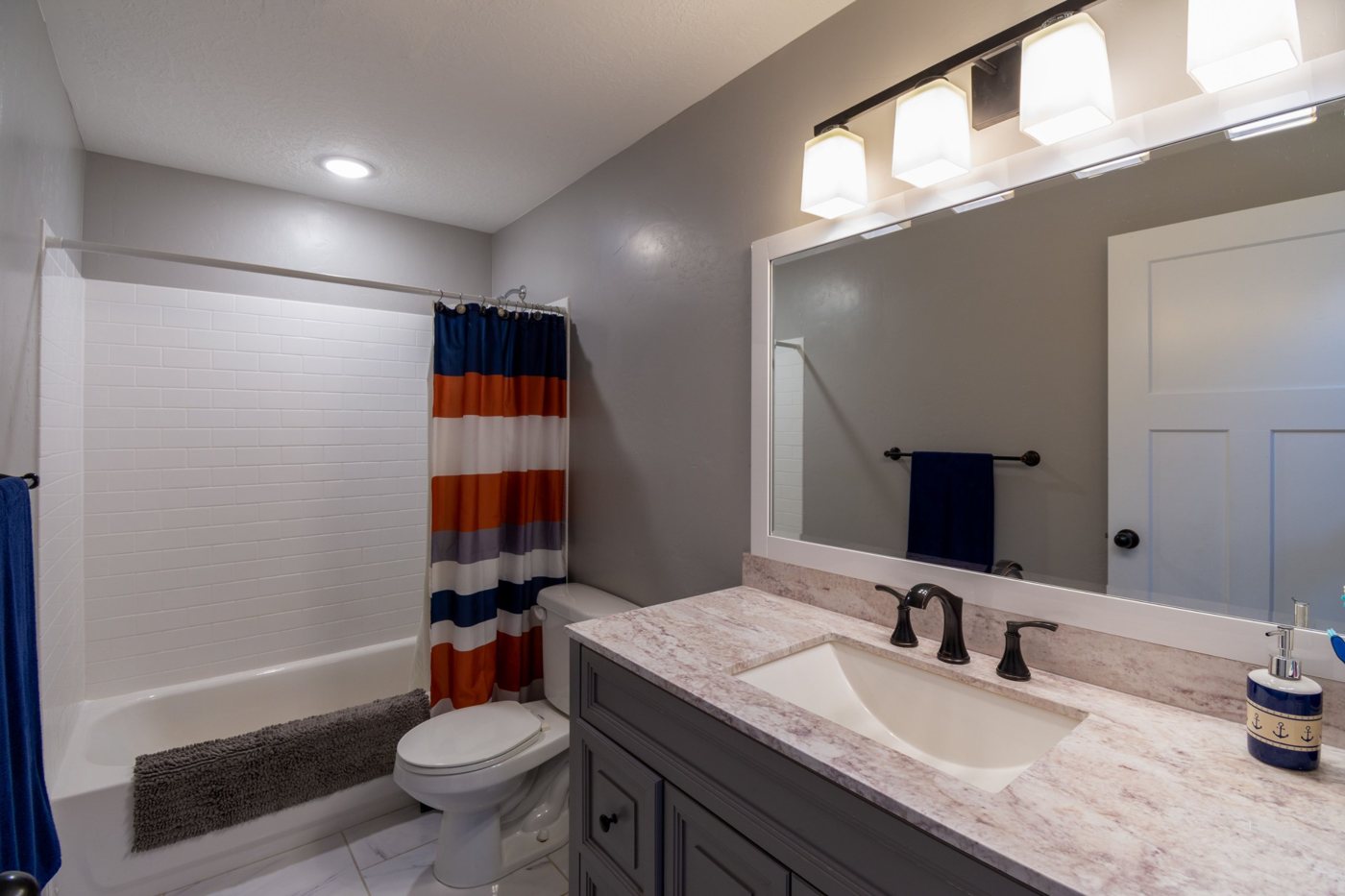 Bathroom with gray vanity, stone countertop, framed mirror and white subway-tile tub surround