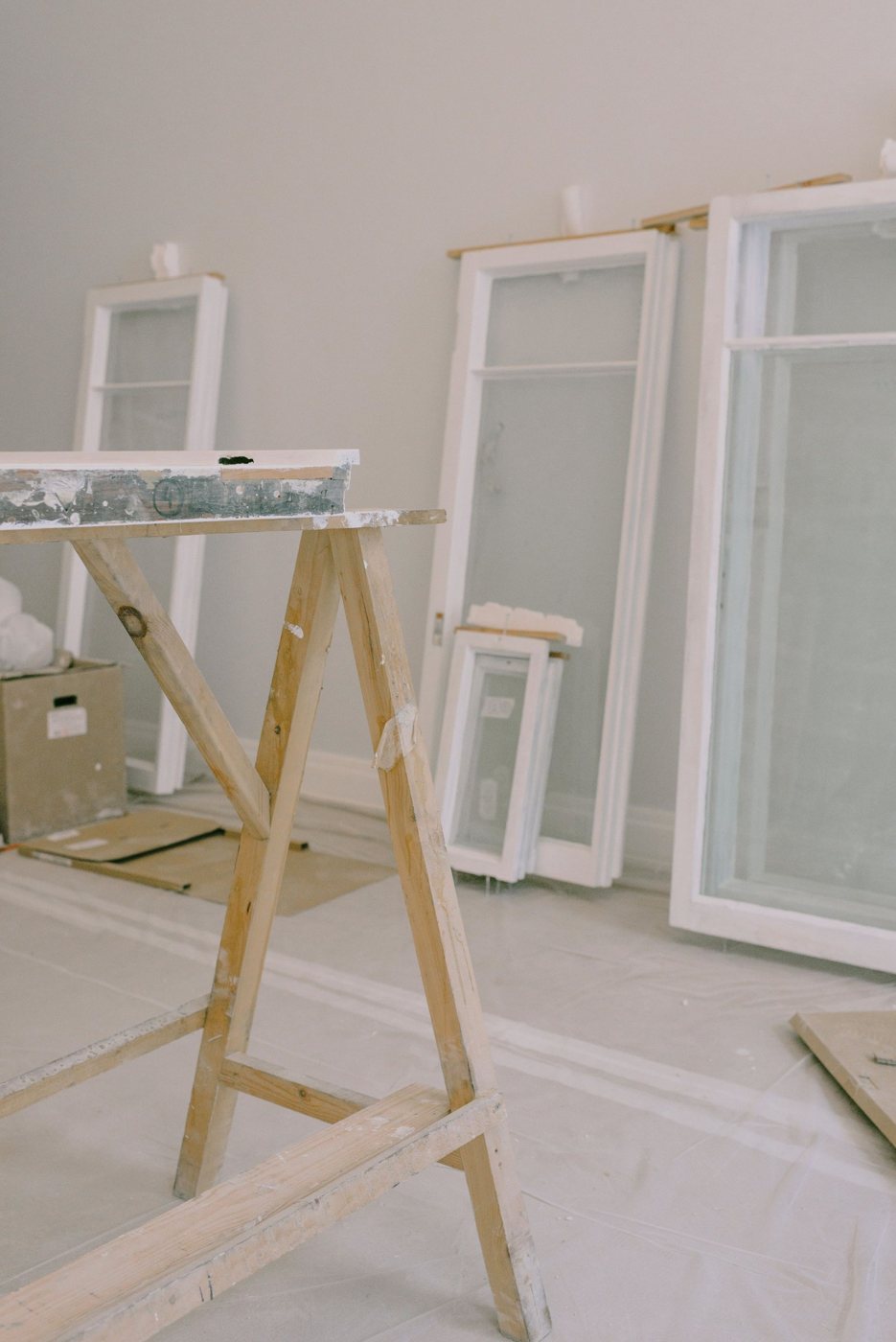 Sawhorse and window sashes being restored in a room prepped with drop cloths