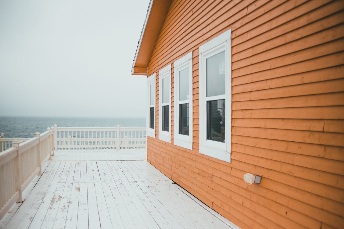 House exterior with clapboard siding and white-trimmed double-hung windows beside a deck